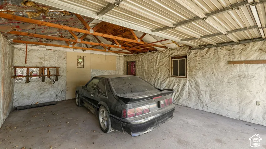 Enclosed garage space featuring exposed timber roof trusses, industrial-style wall insulation, a concrete floor, and an exterior-facing window