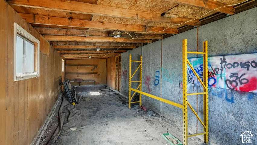 Interior space featuring exposed wood ceiling joists, wood-panel siding, concrete-finish wall panels, and windows
