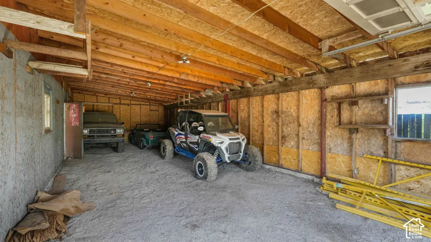 Spacious garage featuring exposed wood beam ceiling construction, oriented strand board wall paneling, and concrete flooring
