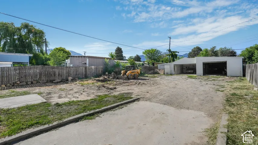 Expansive outdoor space featuring a detached multi-bay garage, concrete hardscaping, and wooden perimeter fencing