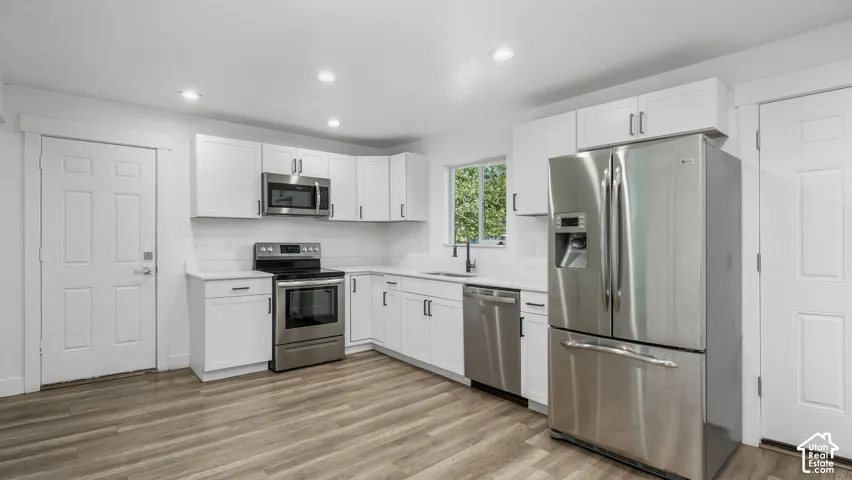 Kitchen featuring white Shaker-style cabinetry, stainless steel appliances, neutral stone-finish countertops, wood-finish flooring, and recessed ceiling lighting