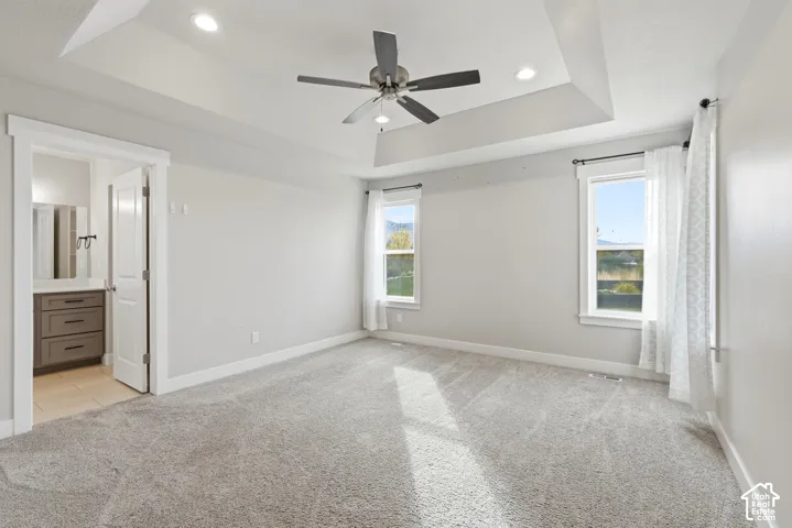 Tray ceiling with recessed lighting and a central ceiling fan, neutral wall-to-wall carpeting, and double-hung windows with exterior mountain scenery