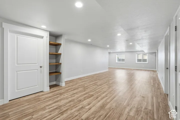 Spacious interior featuring wood-finish flooring, recessed lighting, built-in wooden shelving, and two egress-style windows