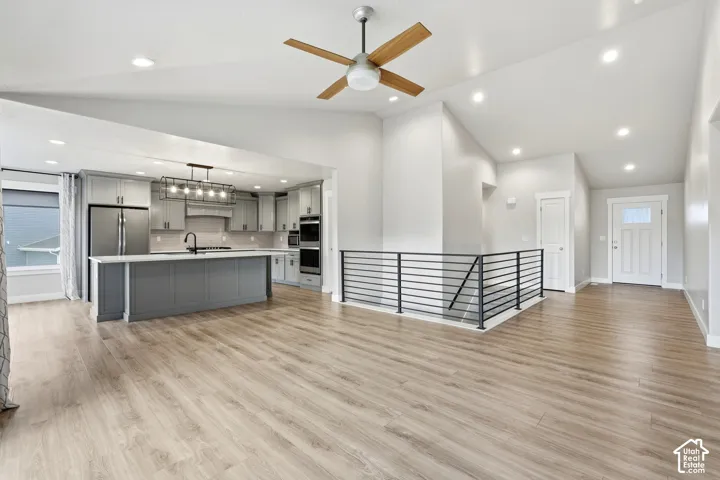 Vaulted ceilings featuring recessed lighting, wood-finish flooring, kitchen island with integrated sink, stainless steel built-in appliances, and matte black horizontal stair railing