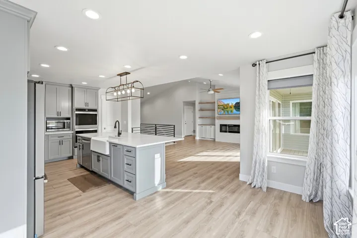 Kitchen featuring custom gray cabinetry, quartz-topped center island with farmhouse sink, recessed lighting, wood-finish flooring, and built-in wall oven