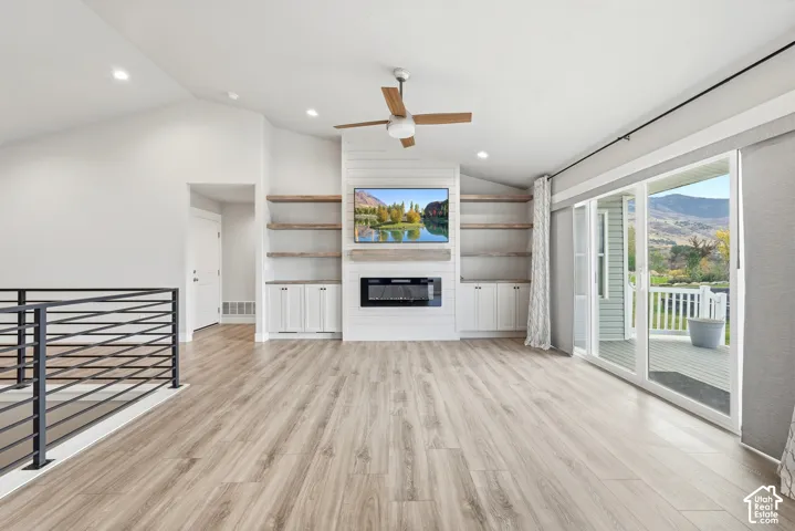 Vaulted ceilings featuring recessed lighting, wood-finish flooring, a floor-to-ceiling shiplap fireplace surround with built-in cabinetry and open shelving, a metal cable railing, and sliding glass doors