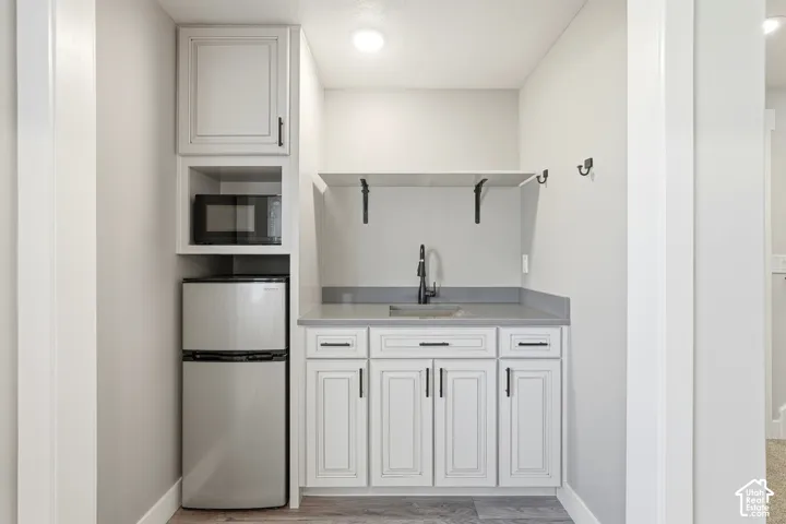 Wet bar featuring white cabinetry, solid-surface countertop, undermount sink with a gooseneck faucet, matte black hardware, and open shelving