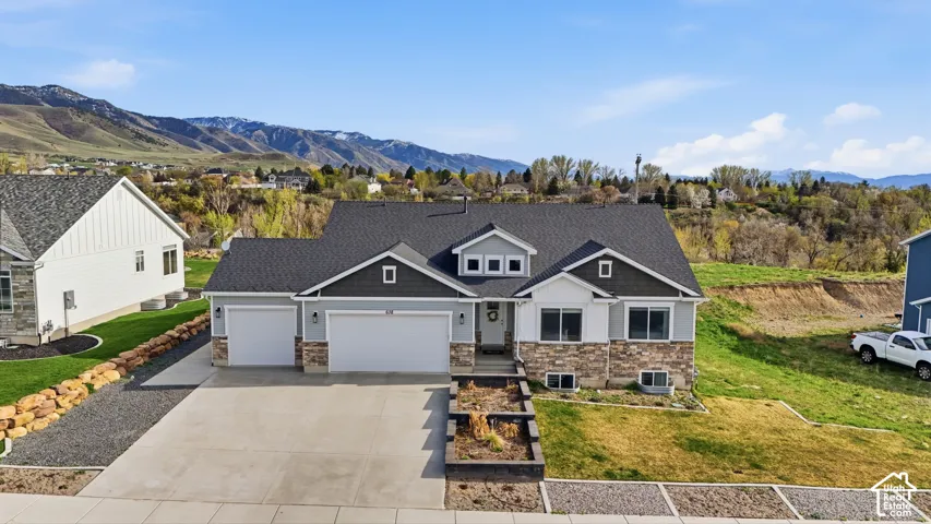 Exterior featuring multi-gabled rooflines, stone veneer masonry, horizontal lap siding, a three-car garage, and a concrete driveway set against a mountain backdrop