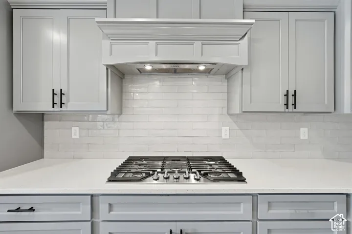 Shaker-style cabinetry with matte black hardware, integrated range hood, white subway tile backsplash, quartz countertop, and stainless steel gas cooktop
