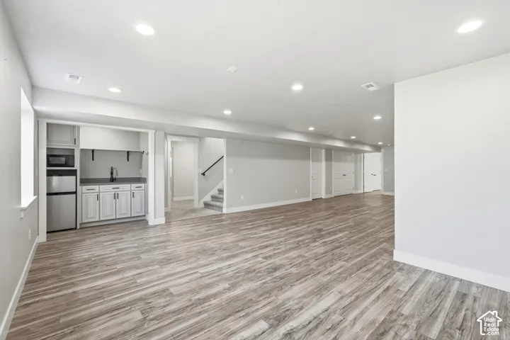 Open-concept interior featuring wood-finish flooring, recessed lighting, and a kitchenette with shaker-style cabinetry, a stone countertop, and a built-in beverage refrigerator