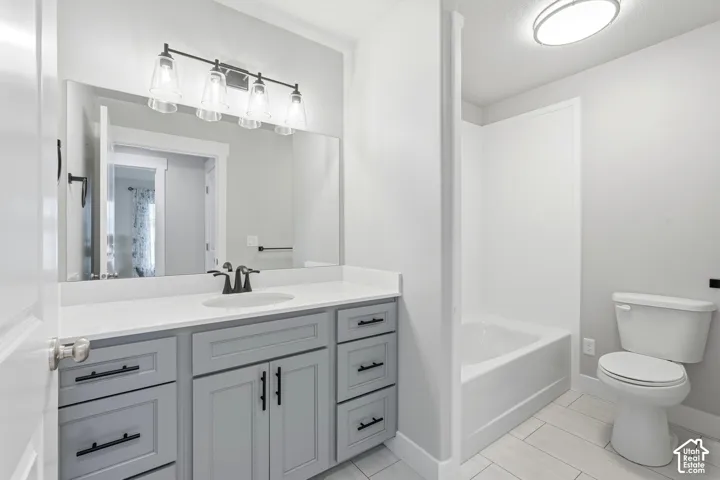 Bathroom vanity featuring grey shaker-style cabinetry, white countertop with integrated sink, matte black hardware, multi-light fixture, and tub-shower combination with tile flooring