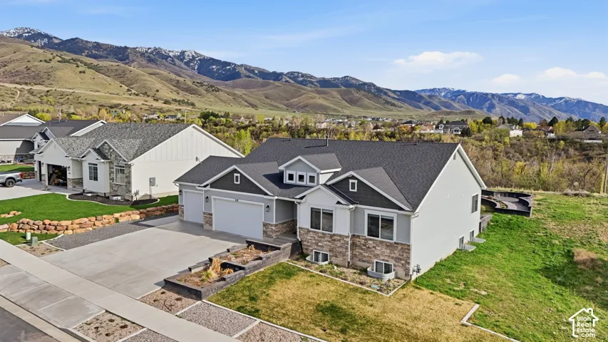 Multi-level residence featuring a stone and horizontal siding exterior, attached three-car garage, concrete driveway, and tiered stone garden walls set against a mountain backdrop