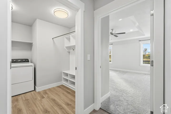 Laundry room featuring wood-finish flooring, white built-in cabinetry, and integrated shelving, with a separate room showcasing a tray ceiling and carpeted flooring