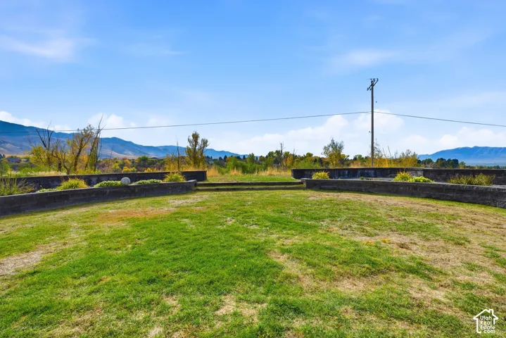 Outdoor grounds featuring a raised stone retaining wall, terraced landscape design, grass lawn, and mountain scenery