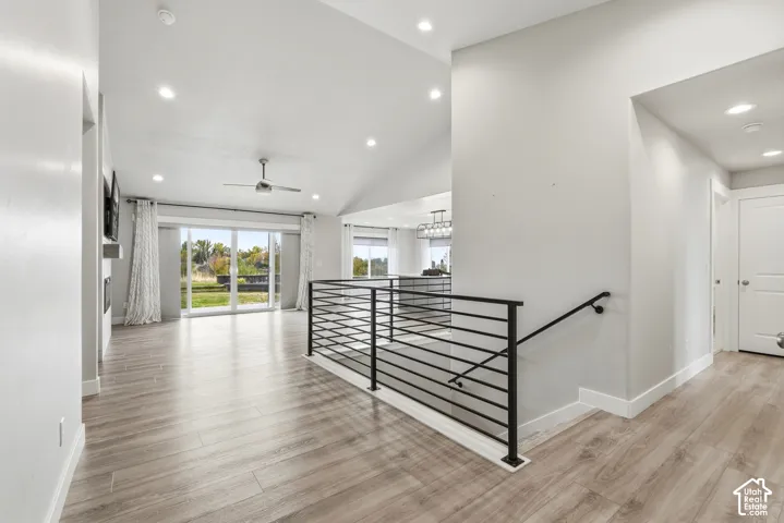 Open-concept interior featuring vaulted ceilings, wood-finish flooring, recessed lighting, and a modern horizontal metal railing