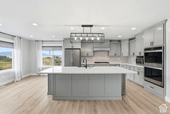 Kitchen featuring a central island with quartz countertops, custom grey cabinetry, stainless steel double wall ovens, wood-finish flooring, and industrial-style pendant lighting