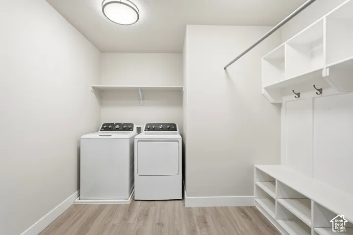 Laundry room featuring wood-finish flooring, white built-in shelving, a metal hanging rod, and wall-mounted storage hooks