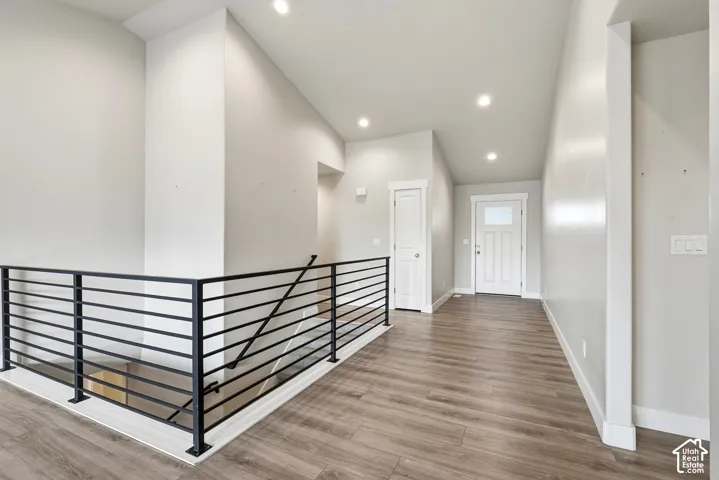 Interior hallway featuring a vaulted ceiling, recessed lighting, wood-finish flooring, and a modern matte black horizontal bar railing