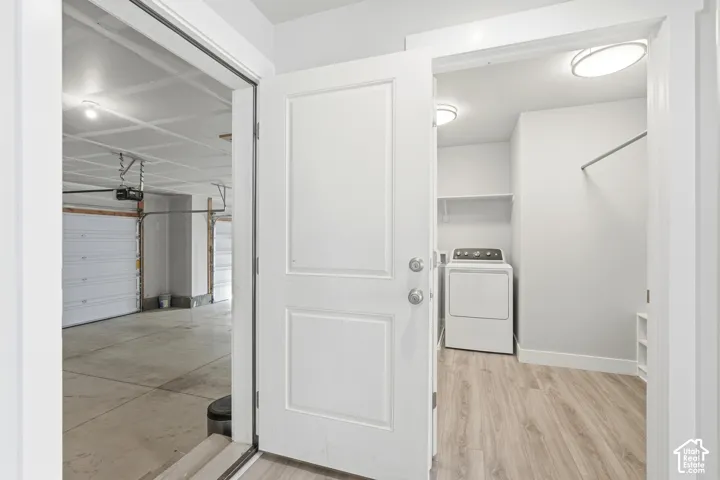 Utility space featuring wood-finish flooring, built-in shelving, a clothes rod, and overhead flush-mount lighting, with entry to a concrete-floor garage