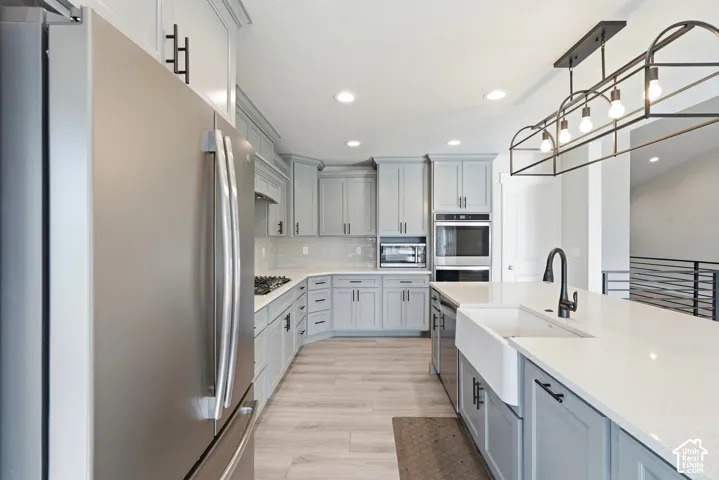 Kitchen featuring shaker-style cabinetry, quartz countertops, farmhouse sink with a pull-down faucet, stainless steel appliances, and wood-finish flooring