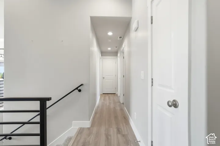 Hallway featuring wood-finish flooring, recessed lighting, and a metal stair railing with horizontal bars, accented by solid-core interior doors with satin nickel hardware
