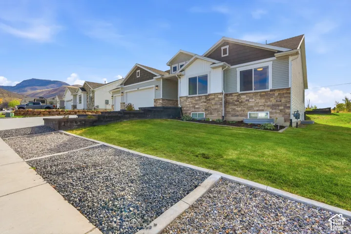 Exterior facade featuring a combination of stone veneer and horizontal siding, asphalt shingle roof, two-car garage, manicured lawn, and mountainous backdrop
