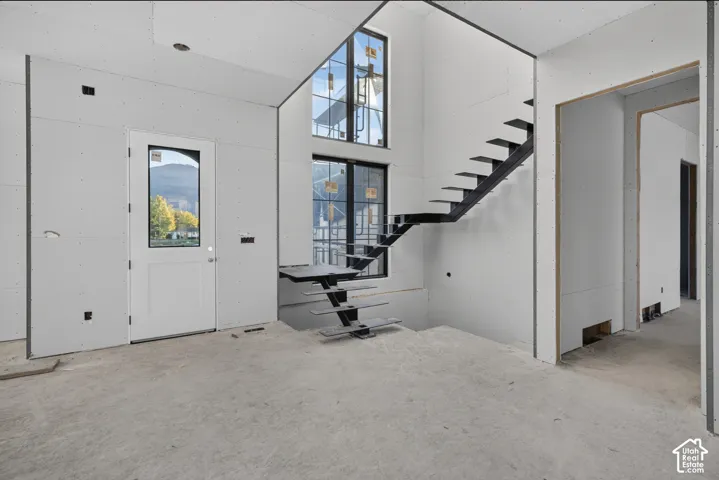 Open-concept interior featuring high ceilings, a custom floating staircase with metal treads, vertical multi-pane windows, and a glass-inset entry door