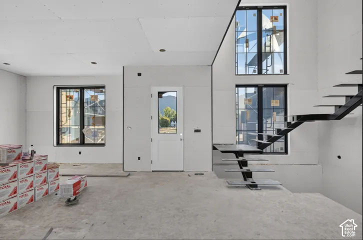 Open-concept interior featuring tall windows with black frames, a minimalist metal staircase, and an exterior door with a glass pane