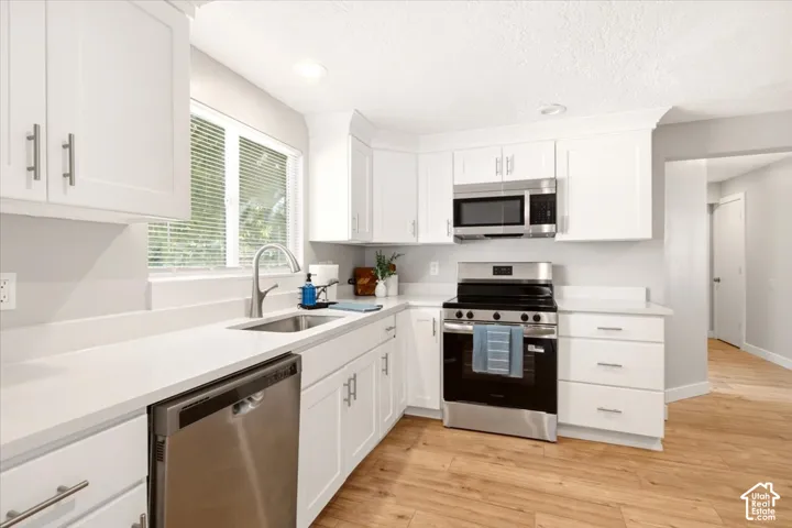 Kitchen featuring white Shaker-style cabinetry, solid-surface countertops, stainless steel appliances, and wood-finish flooring