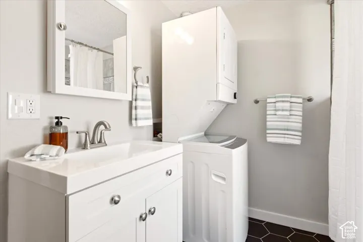 White vanity with integrated sink, brushed nickel faucet, wall-mounted medicine cabinet, stacked laundry center, and dark hexagonal tile flooring