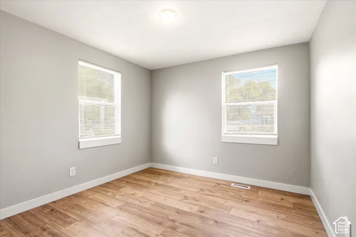 Neutral wall finishes, wood-finish flooring, two dual-pane windows with integrated blinds, and a flush-mount ceiling light