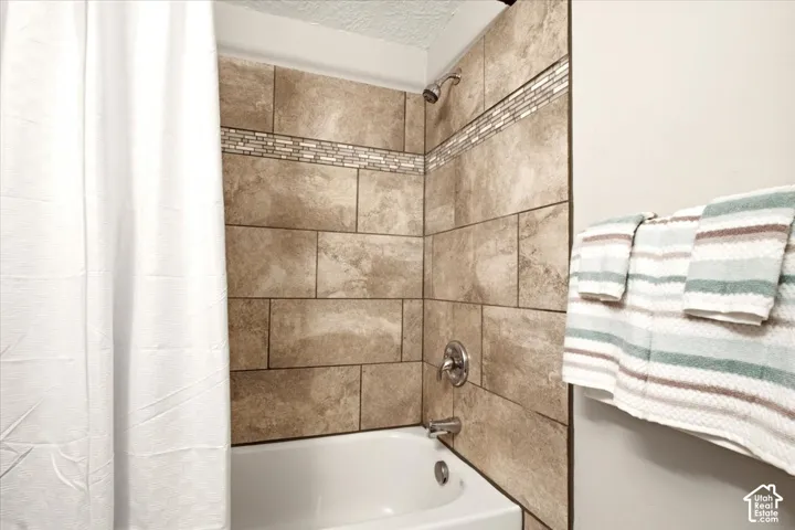 Bathtub featuring large-format neutral tile surround, integrated glass and stone mosaic accent inlay, and polished chrome shower fixtures