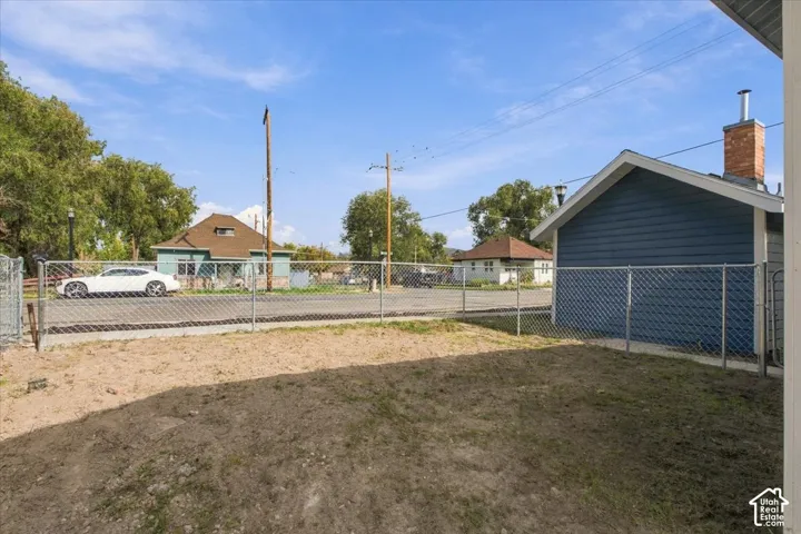 Exterior lot featuring a detached garage with blue horizontal siding and a brick chimney, enclosed by a chain-link fence