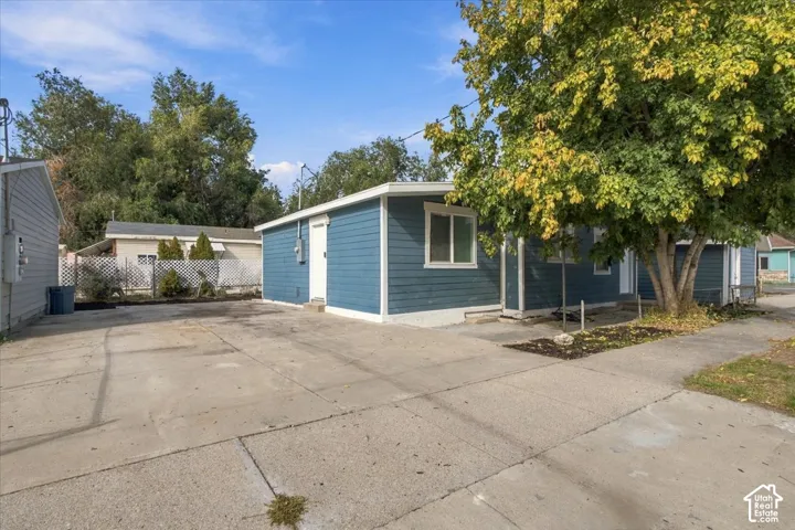 Single-story exterior featuring blue horizontal siding, white trim, concrete driveway, and mature trees