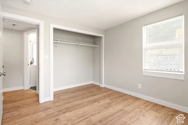 Neutral-toned interior featuring wood-finish flooring, a recessed closet with built-in shelving, and a window with horizontal blinds