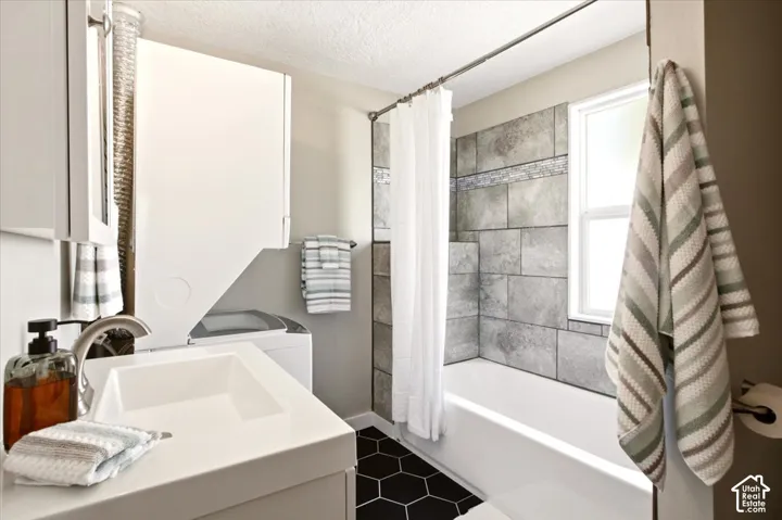 Bathroom featuring a floating vanity with a rectangular basin, geometric black floor tiling, and a tub-shower combination with large-format tile surround and a decorative stone-finish inlay