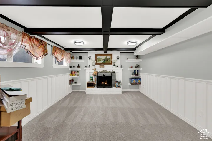 Coffered ceiling with contrasting beams, floor-to-ceiling white wood paneling, fireplace with brick surround and mantel, and built-in floating shelves
