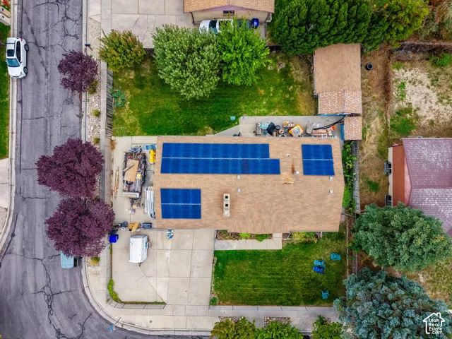 Aerial perspective of the property featuring roof-mounted solar panels, an asphalt shingle roof, a masonry chimney, a concrete driveway, and mature landscaping