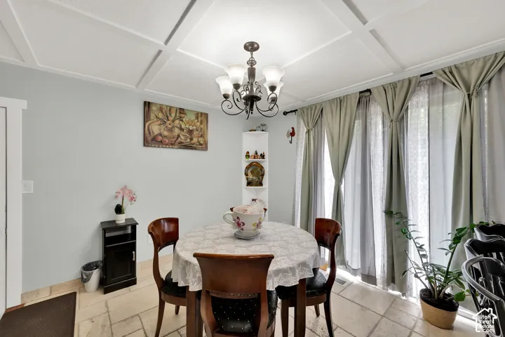 Coffered ceiling, stone-tile flooring, sliding glass doors, and a multi-light metal chandelier