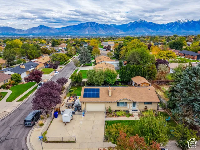 Single-story residence featuring a shingle roof, roof-mounted solar panels, concrete driveway, and mountain backdrop