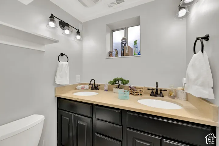 Double vanity featuring dark cabinetry, solid surface countertop with integrated dual sinks, bronze-tone fixtures, and dual wall-mounted light fixtures