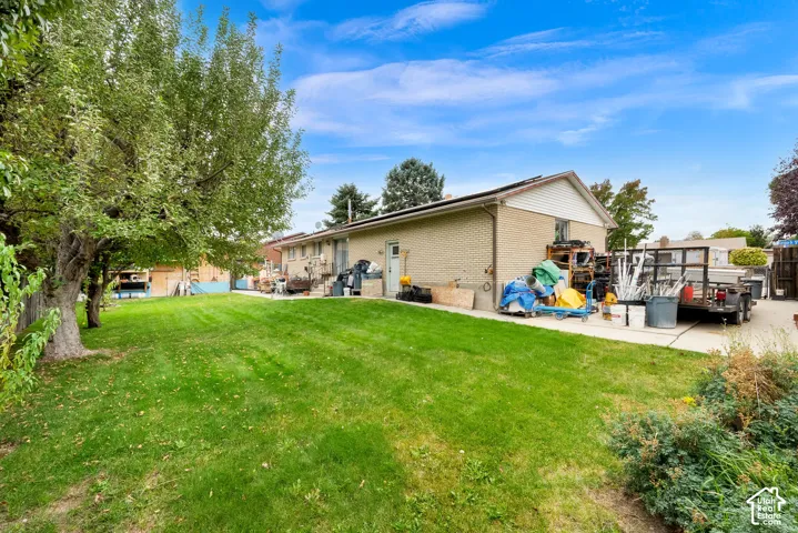 Exterior of the brick residence featuring a concrete patio, expansive lawn, and mature trees