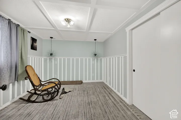 Room featuring a coffered ceiling, board-and-batten wall detailing, carpeted flooring, and dual pendant light fixtures