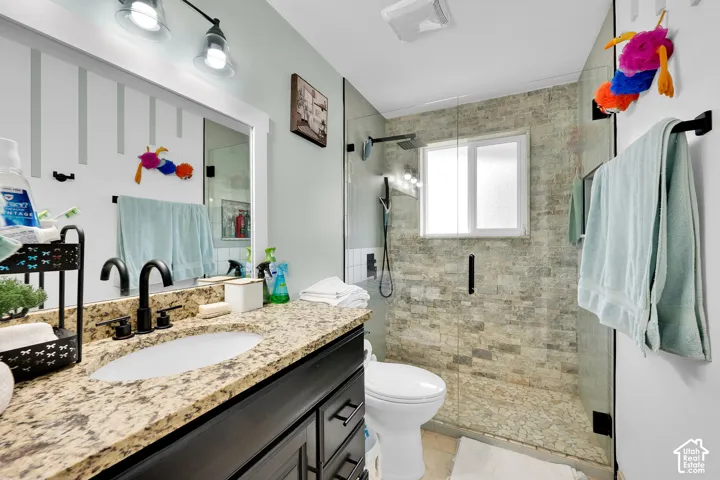 Bathroom featuring a dark wood vanity with a stone countertop, under-mount sink, matte black faucet, and a walk-in shower with natural stone tile walls, a glass enclosure, and a rain-style showerhead
