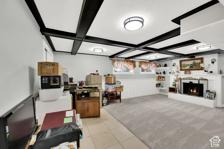 Coffered ceiling with dark-toned beams, white-painted brick fireplace, built-in shelving, wainscoting, and carpeted flooring