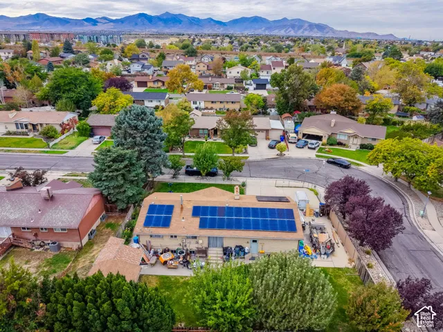 Aerial perspective featuring a single-story residence with rooftop solar panels, a concrete patio, a manicured lawn, and expansive mountain range scenery
