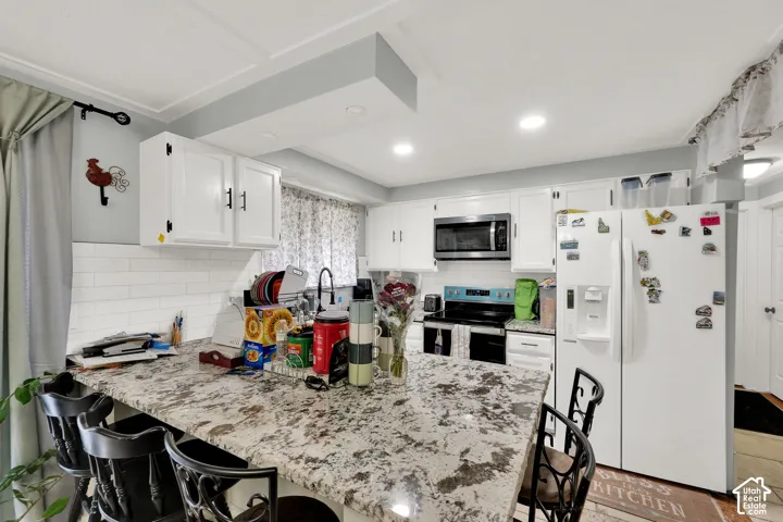 Kitchen featuring white cabinetry, stone-surface breakfast bar, subway tile backsplash, and recessed lighting
