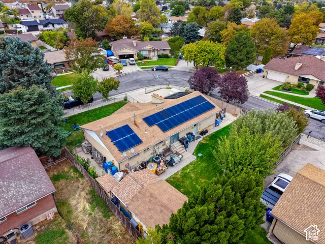 Aerial perspective of a single-story residence featuring rooftop solar panels, a concrete patio, a fenced backyard, and a composition shingle roof