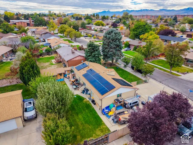 Aerial perspective featuring a shingle roof with integrated solar panels, a concrete driveway, and established landscape greenery