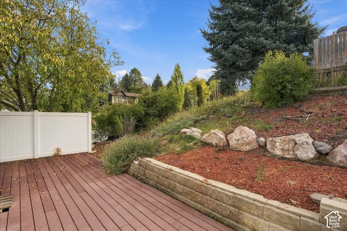 Composite decking, terraced retaining wall, decorative boulder accents, and vinyl perimeter fencing